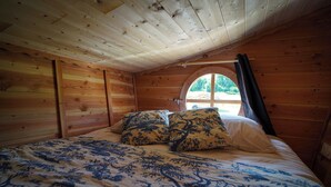 A wooden room with a bed, two pillows, and a window with a view. - The Hobbit House at the Crossroads (Fontenoy)