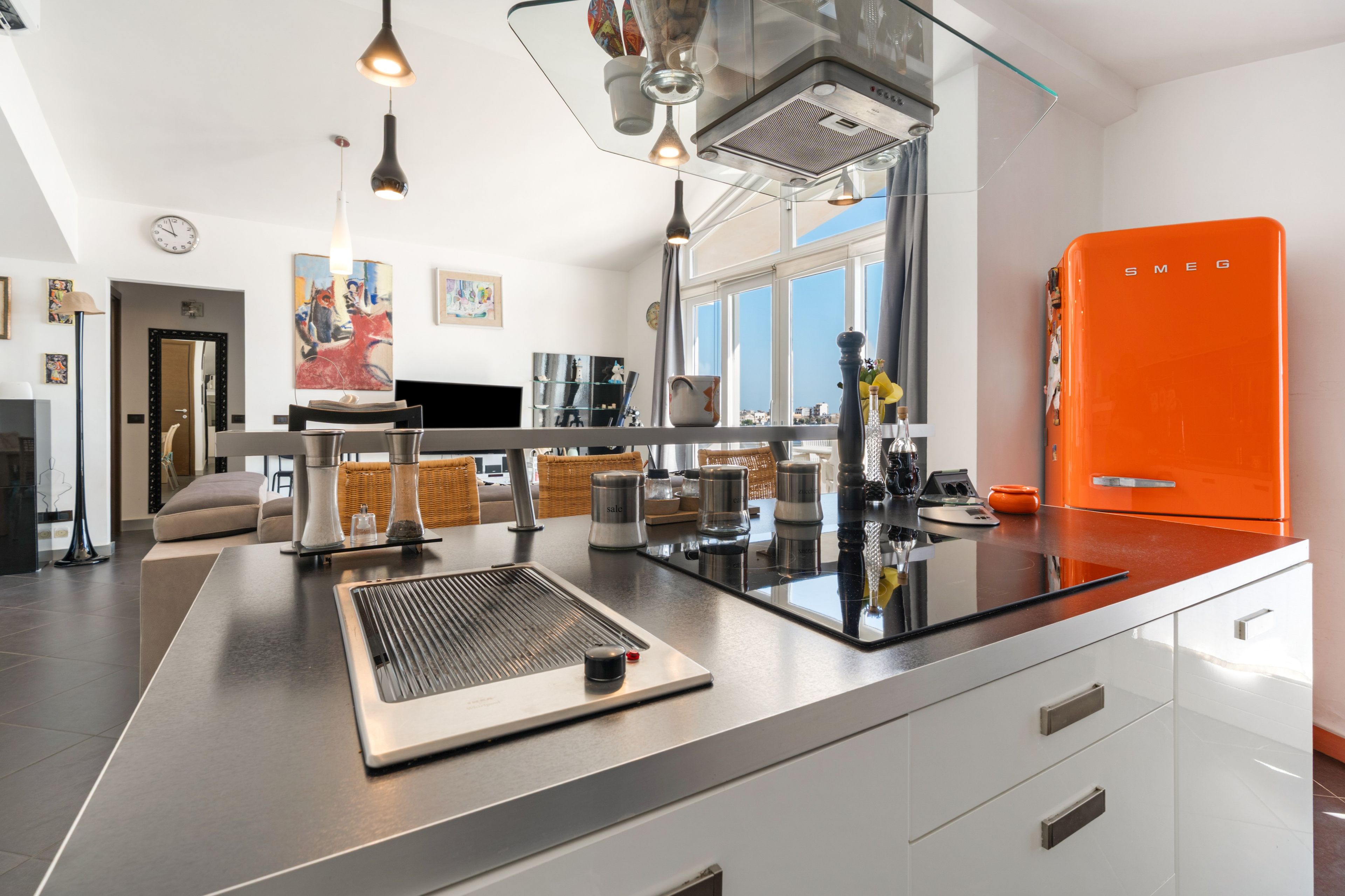 A modern kitchen with a central island, stainless steel appliances, and a bright orange refrigerator.