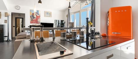 A modern kitchen with a central island, stainless steel appliances, and a bright orange refrigerator.