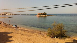 Ein Strand mit einer kleinen Insel, einer Brücke und einer fernen Küstenlinie mit Gebäuden.