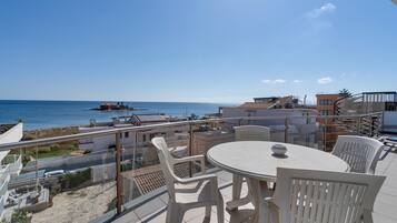 A balcony with a table and chairs, overlooking a coastal area with buildings and a body of water.