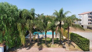 Ein Poolbereich mit Palmen, blauem Himmel und einem Gebäude im Hintergrund.