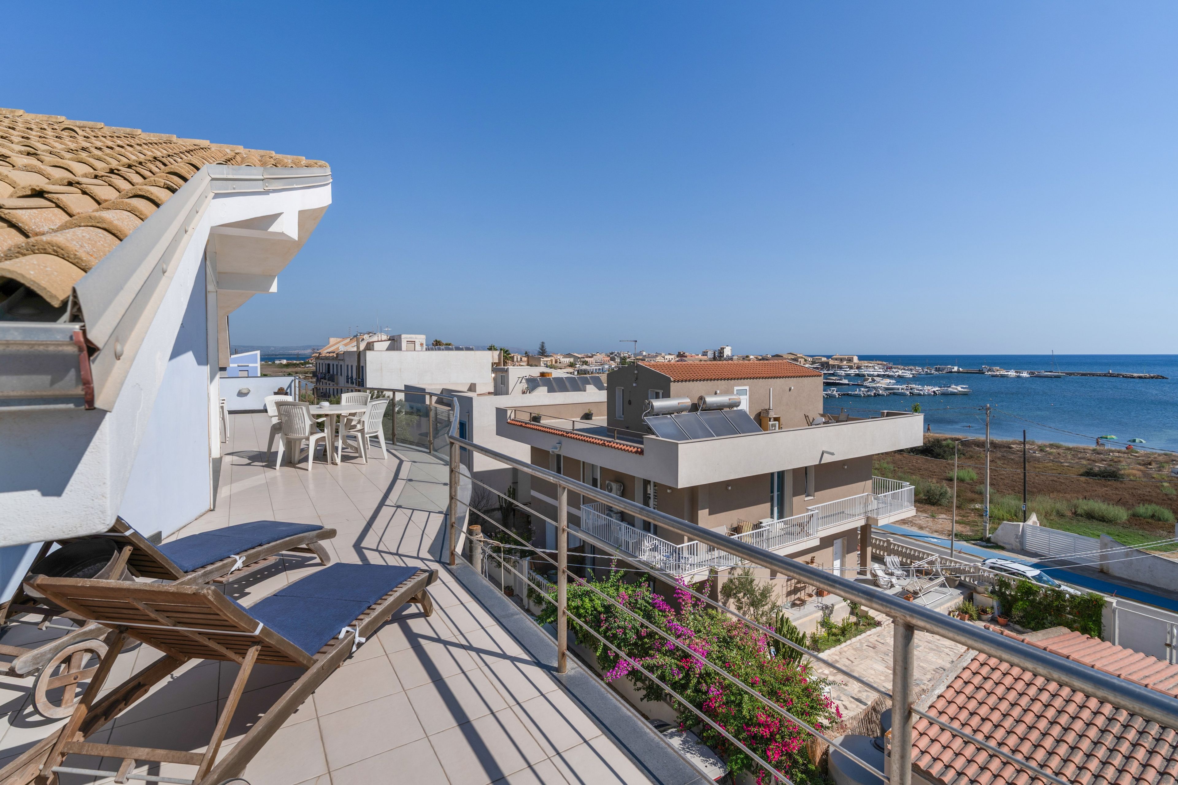 Ein Balkon mit Blick auf das Meer, ein Ziegeldach und ein Gebäude mit flacher Fassade.