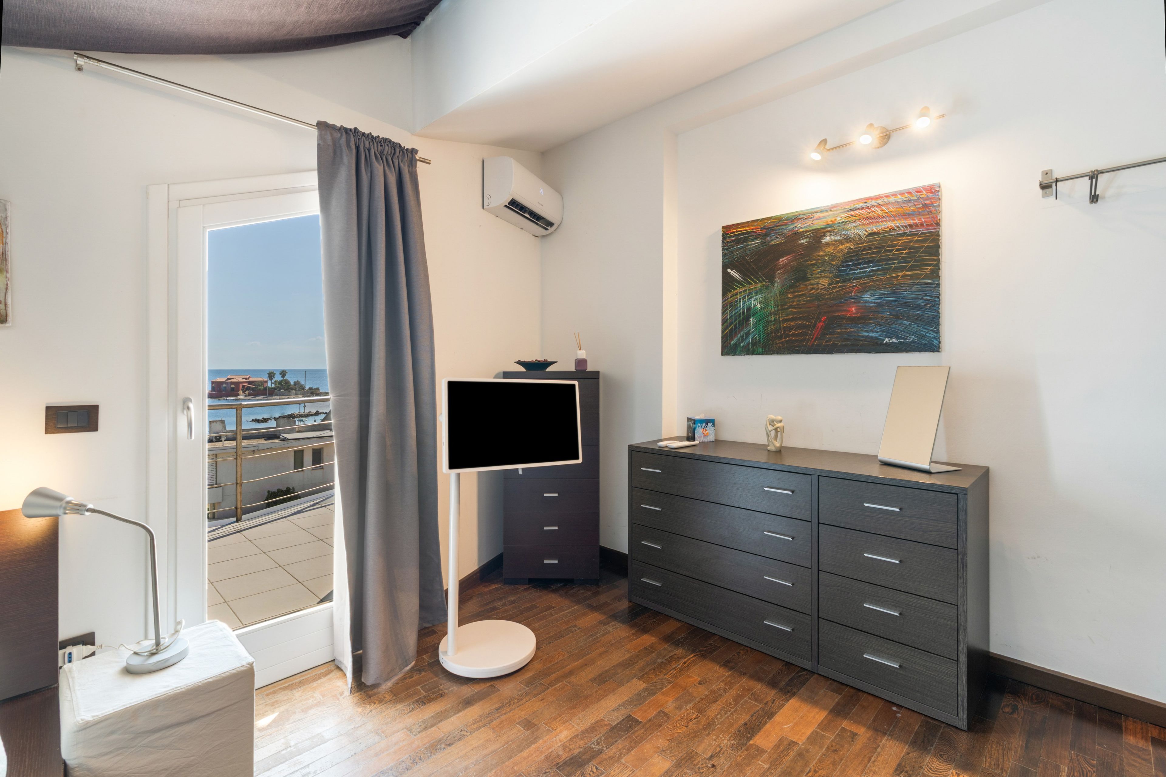 Ein modernes Badezimmer mit Holzboden, einem grauen Schrank, einem Flachbildfernseher und einem Bild an der Wand.