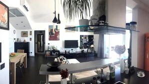 Eine moderne Küche mit einer zentralen Kochinsel, einem Essbereich mit Tisch und Stühlen, einem Fernseher und einem Kühlschrank.