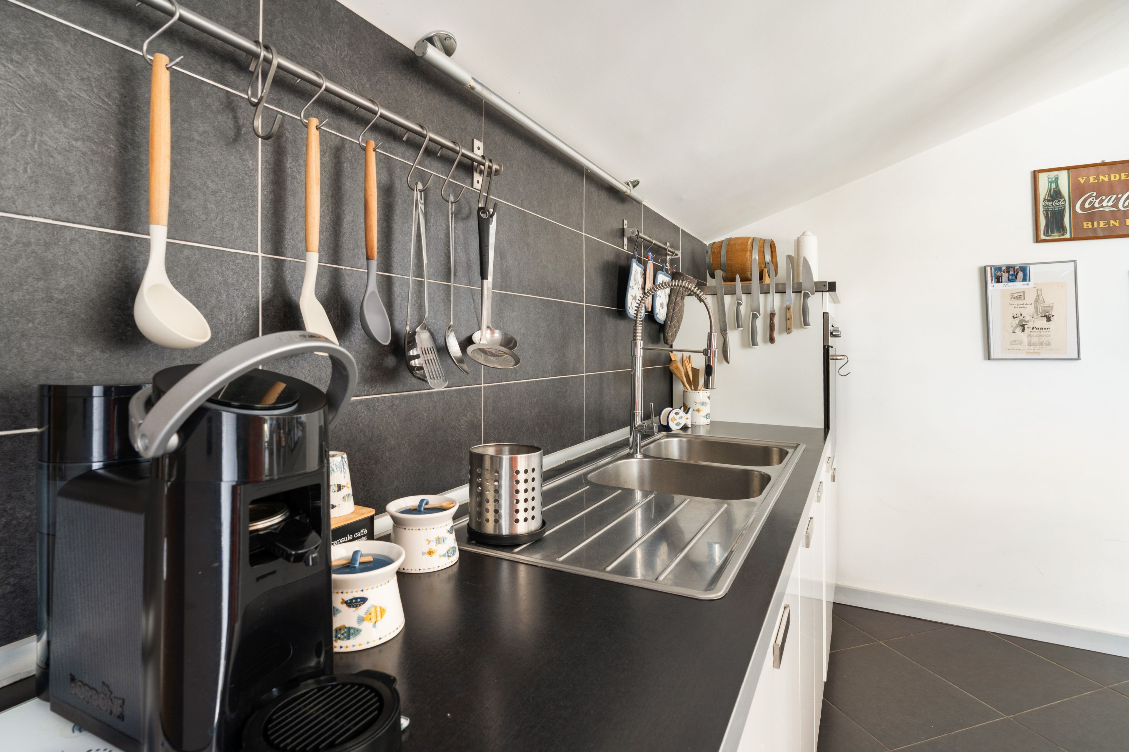 Eine moderne Küche mit schwarzer Arbeitsplatte, Spüle aus Edelstahl und einer Kaffeemaschine.