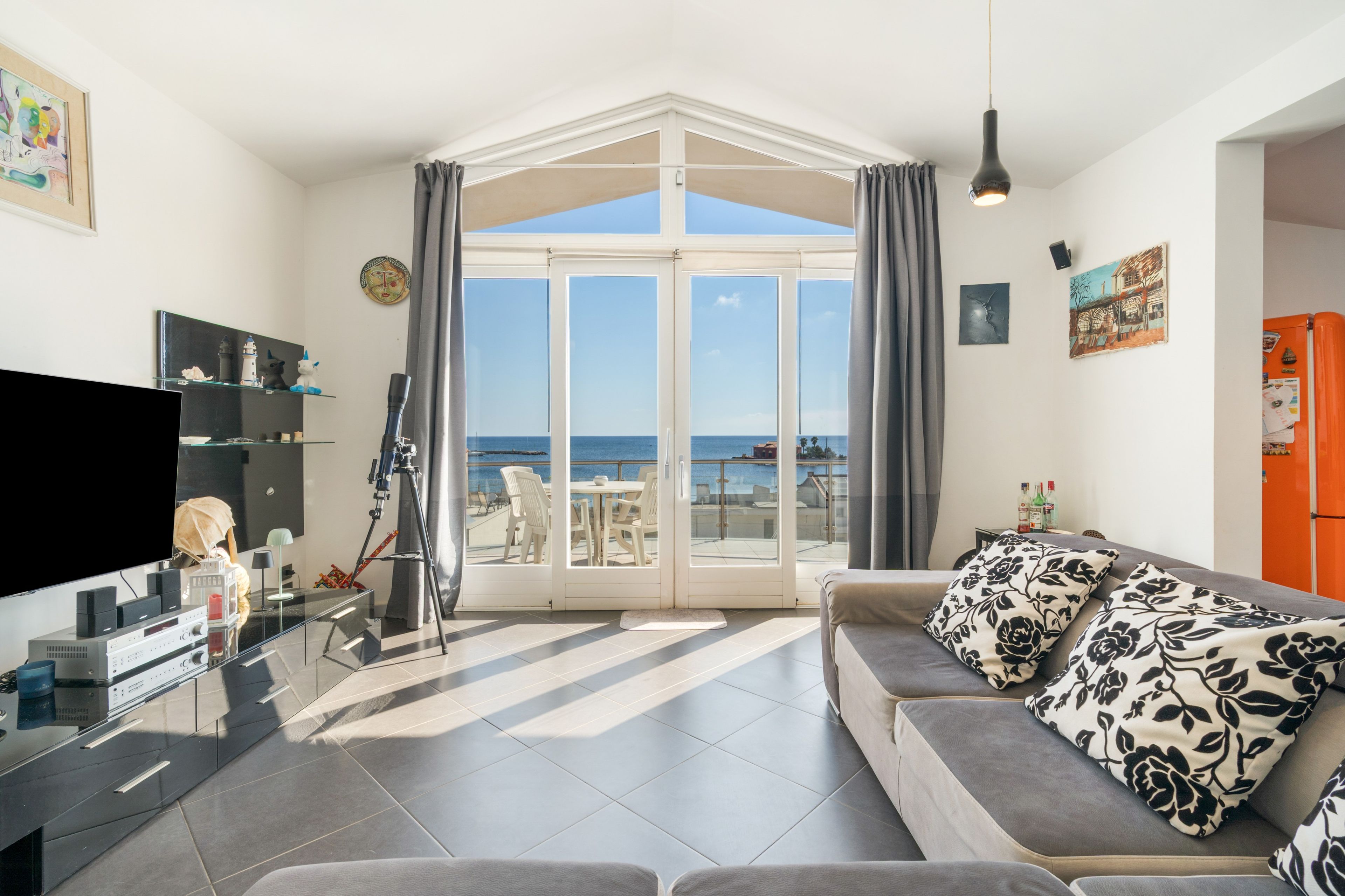 Ein modernes Wohnzimmer mit großem Fenster, einem Flachbildfernseher, einem Teleskop und einer Couch mit gemusterten Kissen.