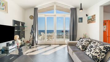 Ein modernes Wohnzimmer mit großem Fenster, einem Flachbildfernseher, einem Teleskop und einer Couch mit gemusterten Kissen.