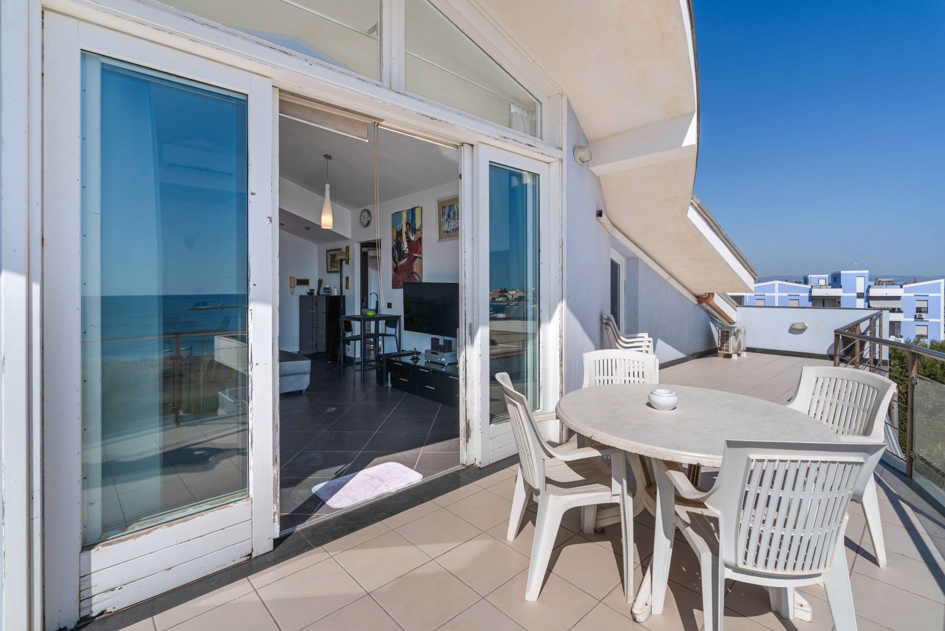 A balcony with a dining table and chairs, a sliding glass door leading to an interior space, and a view of the sea.