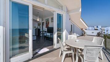 A balcony with a dining table and chairs, a sliding glass door leading to an interior space, and a view of the sea.