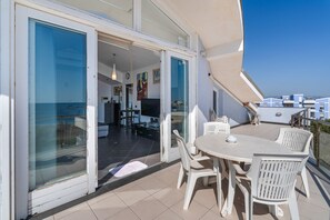 A balcony with a dining table and chairs, a sliding glass door leading to an interior space, and a view of the sea. - Apartment 'Casa Marea Attico' with Sea View, Wi-Fi and Air Conditioning (Marzamemi)