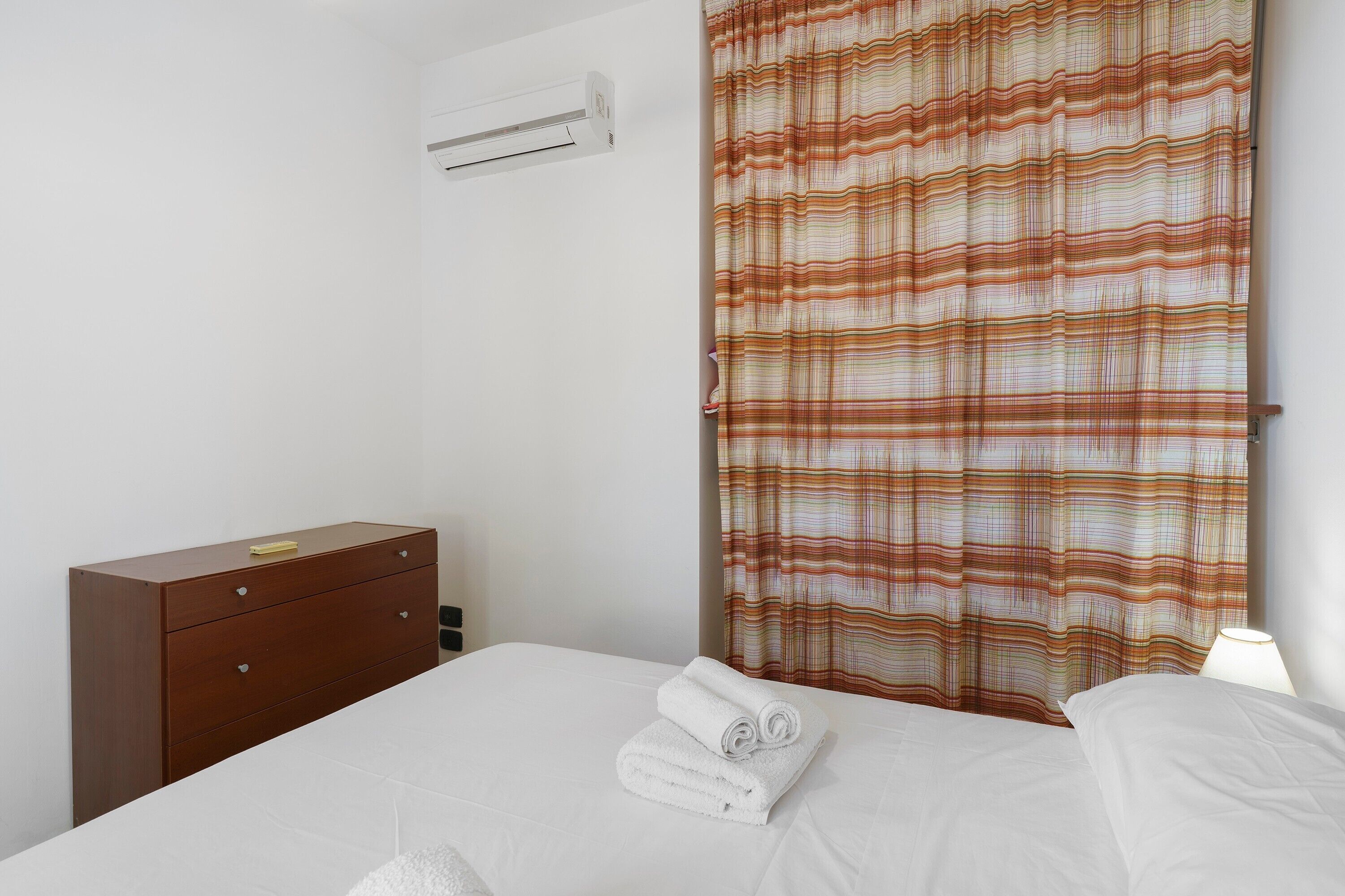 Habitación de hotel con cama, cómoda de madera, unidad de aire acondicionado y cortina estampada.