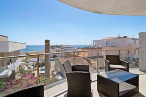 A balcony with wicker furniture, a glass table, and a view of the sea and buildings. - Casa Marea Second Floor with Sea View, Wi-Fi and Air Conditioning (Marzamemi)