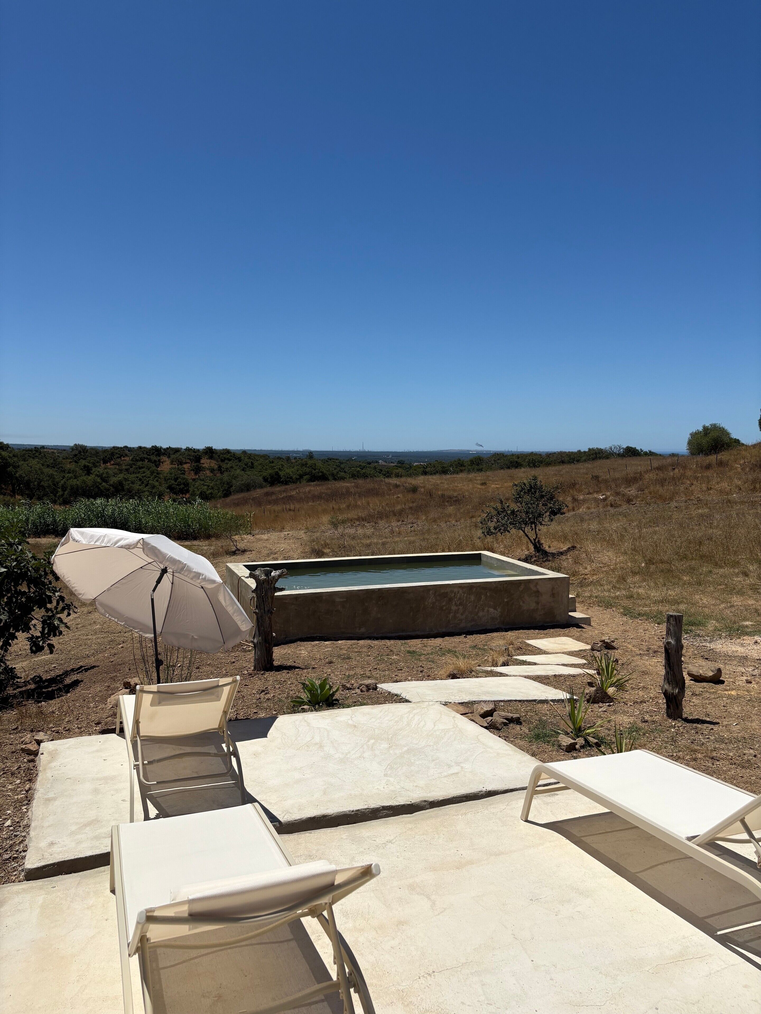 Un patio con sillones de descanso, una piscina y vistas del paisaje.