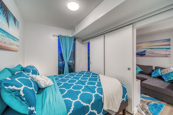 A bedroom with a bed, a sofa, and a view of the sea through a window.