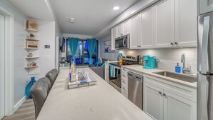 Una cocina moderna con armarios blancos, electrodomésticos de acero inoxidable y un comedor con mesa y sillas blancas.