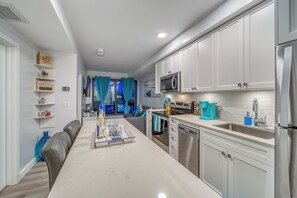 A modern kitchen with white cabinets, stainless steel appliances, and a dining area with a white table and chairs. - Steps to Downtown Oasis 2BR 3 beds Sleeps 6 Underground Free Parking (Calgary)