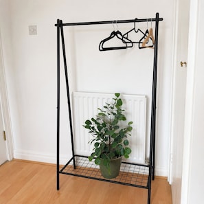 A black metal drying rack with a potted plant and hangers against a white wall. - 3BR Hastings House | Contractor Friendly (Sunderland)