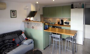 Eine kompakte Küche mit einer zentralen Kochinsel, Barhocker, einem Backofen und einem Kühlschrank.