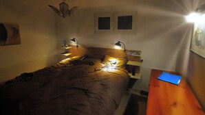 Un dormitorio con una cama, lámparas de noche, una mesita de noche de madera y una carpeta azul sobre la mesita.