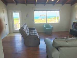 Olohuoneessa on puulattia, harmaa sohva, vaaleansininen nojatuoli ja televisio.