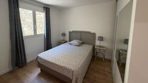 A bedroom with a bed, two bedside tables, a window with curtains, and a mirror. - Charming apartment in the hills above Erbalunga (Brando)