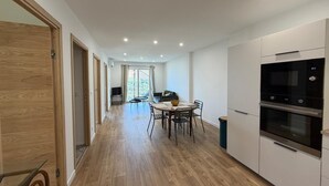 A modern kitchen with a dining area, wooden flooring, and a view through a glass door. - Charming apartment in the hills above Erbalunga (Brando)