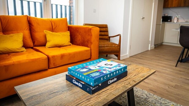 Ein Wohnzimmer mit einem orangefarbenen Sofa, einem Holztisch und dem Spiel 'SCRABBLE' darauf.
