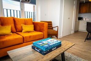Ein Wohnzimmer mit einem orangefarbenen Sofa, einem Holztisch und dem Spiel 'SCRABBLE' darauf.