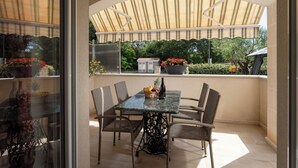 Eine überdachte Terrasse mit Tisch und Stühlen, einem Blumentopf und Blick auf Grünflächen.