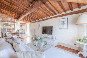 Amplia sala de estar con techo alto, televisor, mesa de comedor y cocina al fondo.