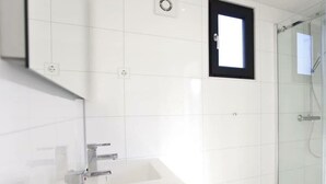 Un baño moderno con cabina de ducha de vidrio, un lavabo blanco y una ventana pequeña.