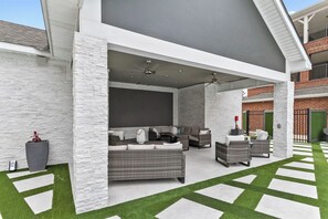 Ein Terrassenbereich im Freien mit Korbmöbeln, Kunstgrashalm und einer weißen Steinwand.