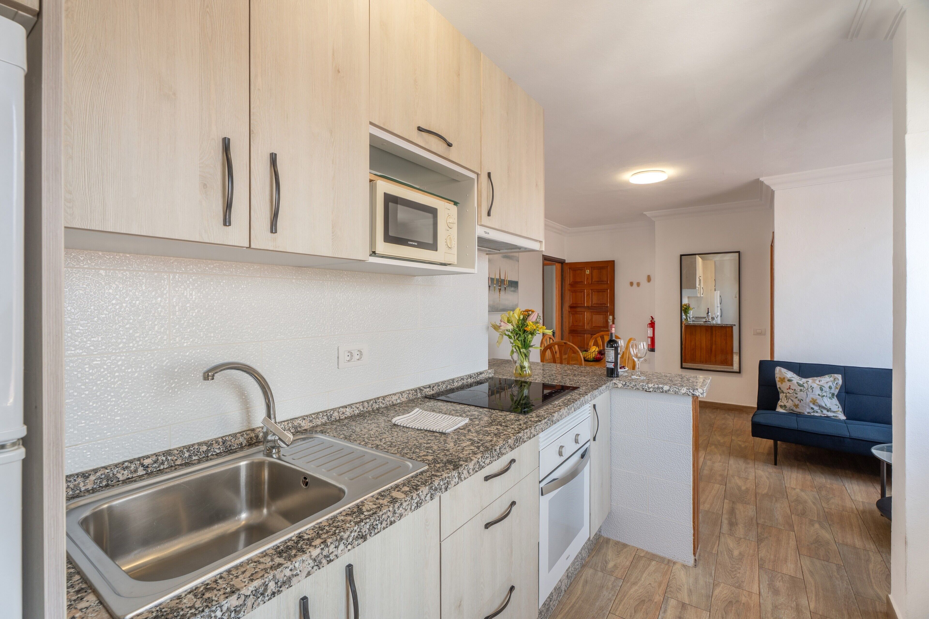 A kitchen with granite countertops, stainless steel sink, wooden cabinets, a microwave, and a built-in oven.