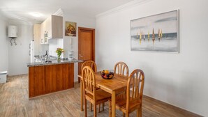 Una cocina con armarios de madera, una mesa de comedor con sillas, un frutero y un cuadro en la pared.