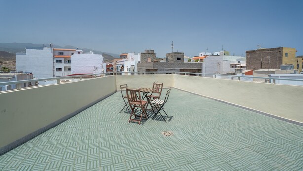 Terraza en la azotea con una mesa y sillas, con vistas a un paisaje urbano lleno de edificios.