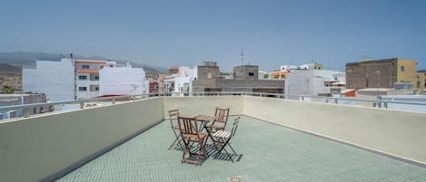 A rooftop terrace with a table and chairs, overlooking a cityscape with various buildings.