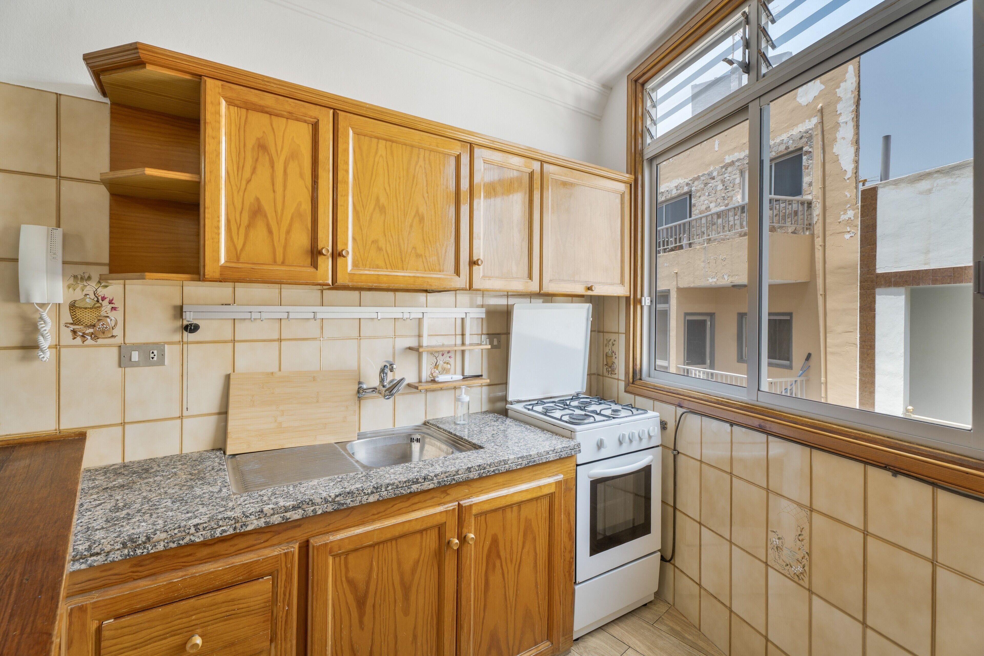 Una cocina con armarios de madera, encimera de granito, estufa y ventana con vistas a edificios.