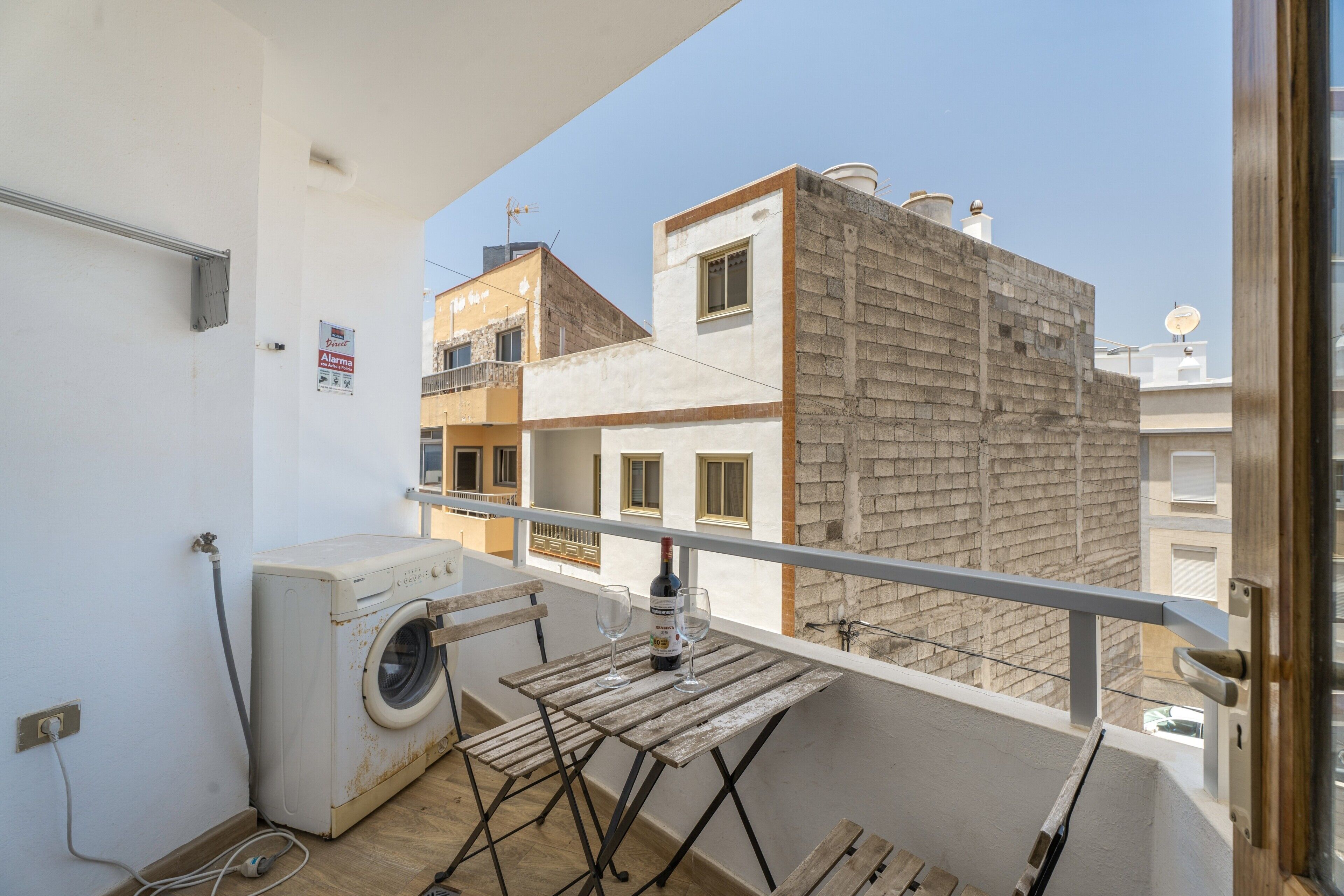 Ein Balkon mit Waschmaschine, Wäscheständer und einem Weinglas.
