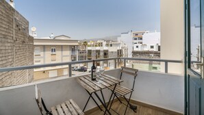 Un balcón con una mesa y sillas de madera, con vistas a una zona residencial con edificios y un cielo despejado.