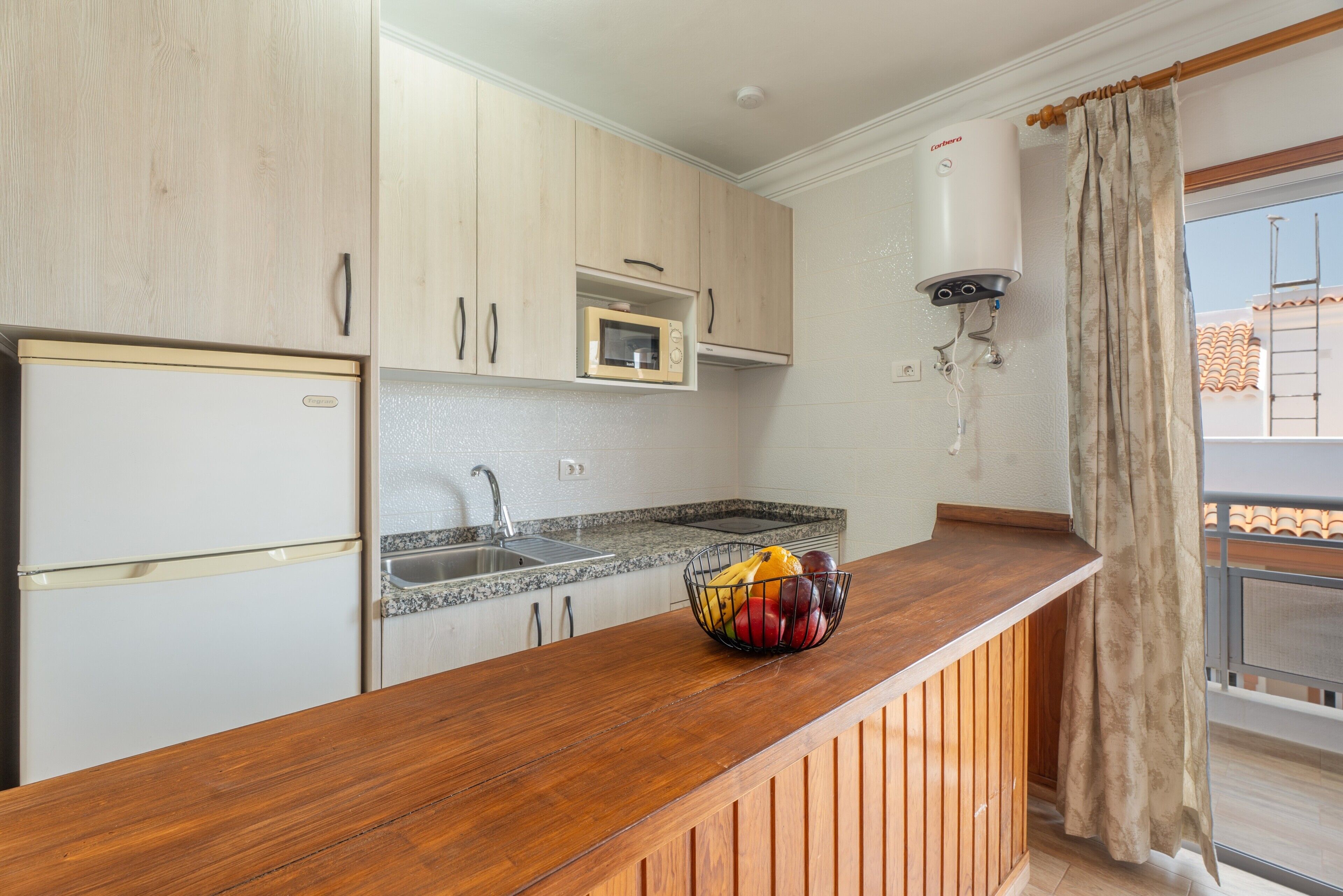 A kitchen with wooden cabinets, a microwave, a sink, and a wooden countertop with a fruit bowl.