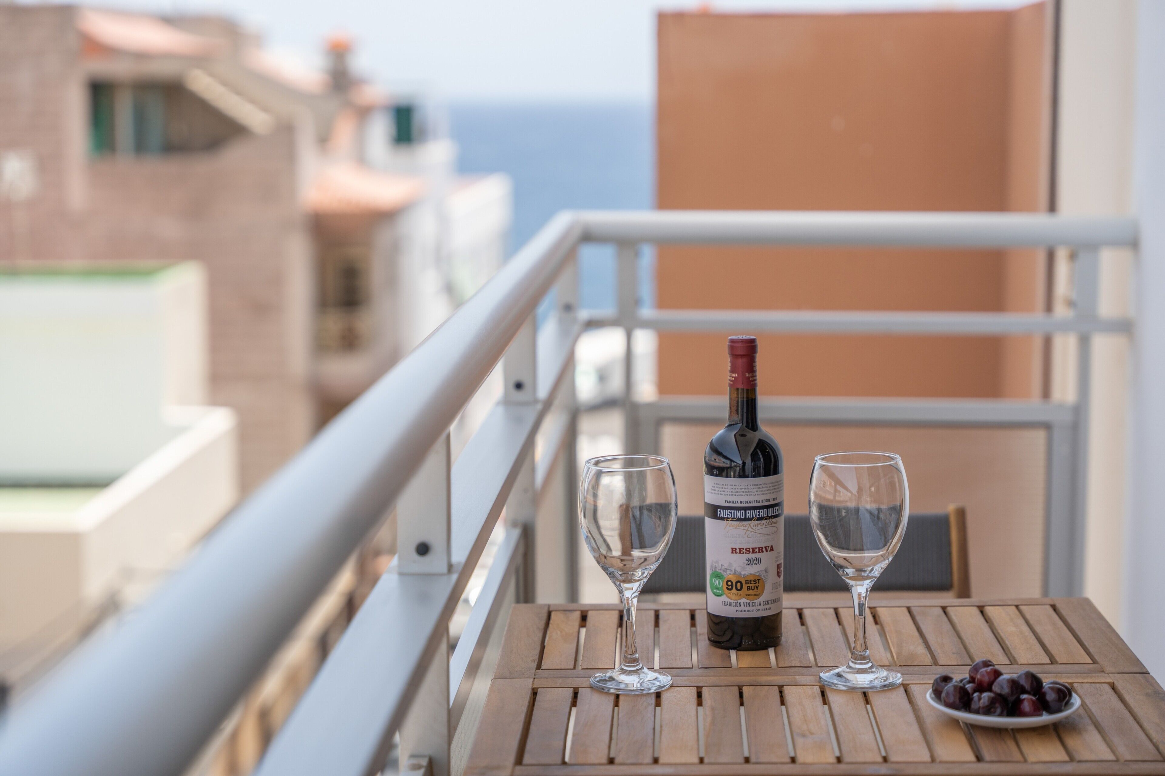 A balcony with a bottle of wine, two glasses, and a plate of grapes.