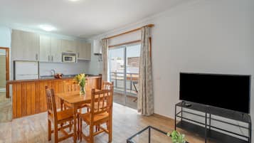 Una cocina moderna con armarios de madera, una mesa de comedor con sillas, un microondas empotrado y un televisor sobre un mueble.