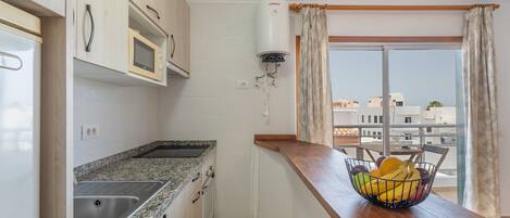 A kitchen with a microwave, a water heater, and a fruit basket on the counter.