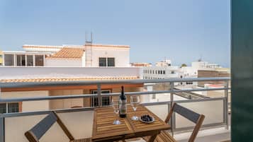 En balkon med et bord, to stole, en flaske vin og en tallerken med druer.