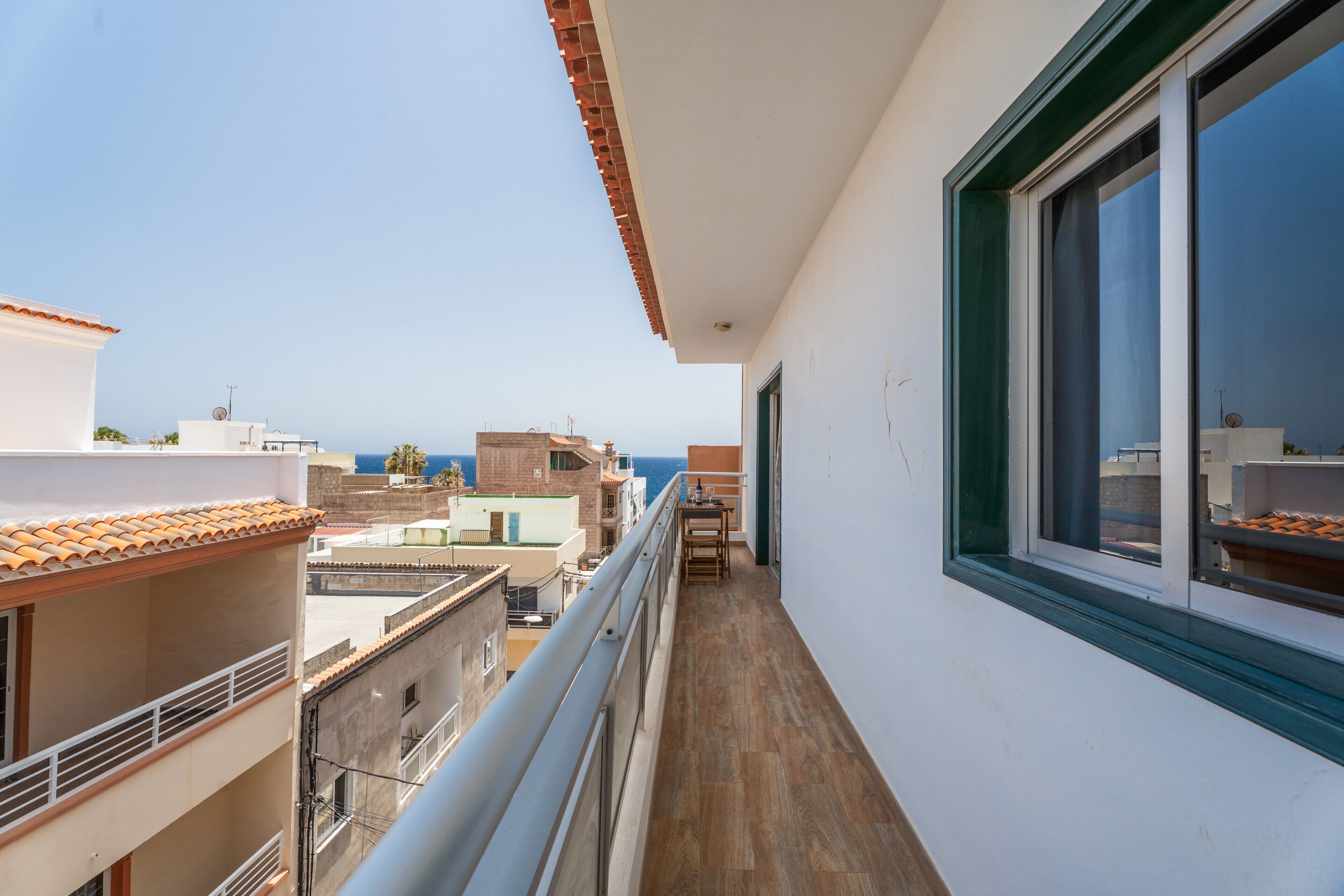 A narrow balcony with a view of the sea and other buildings.
