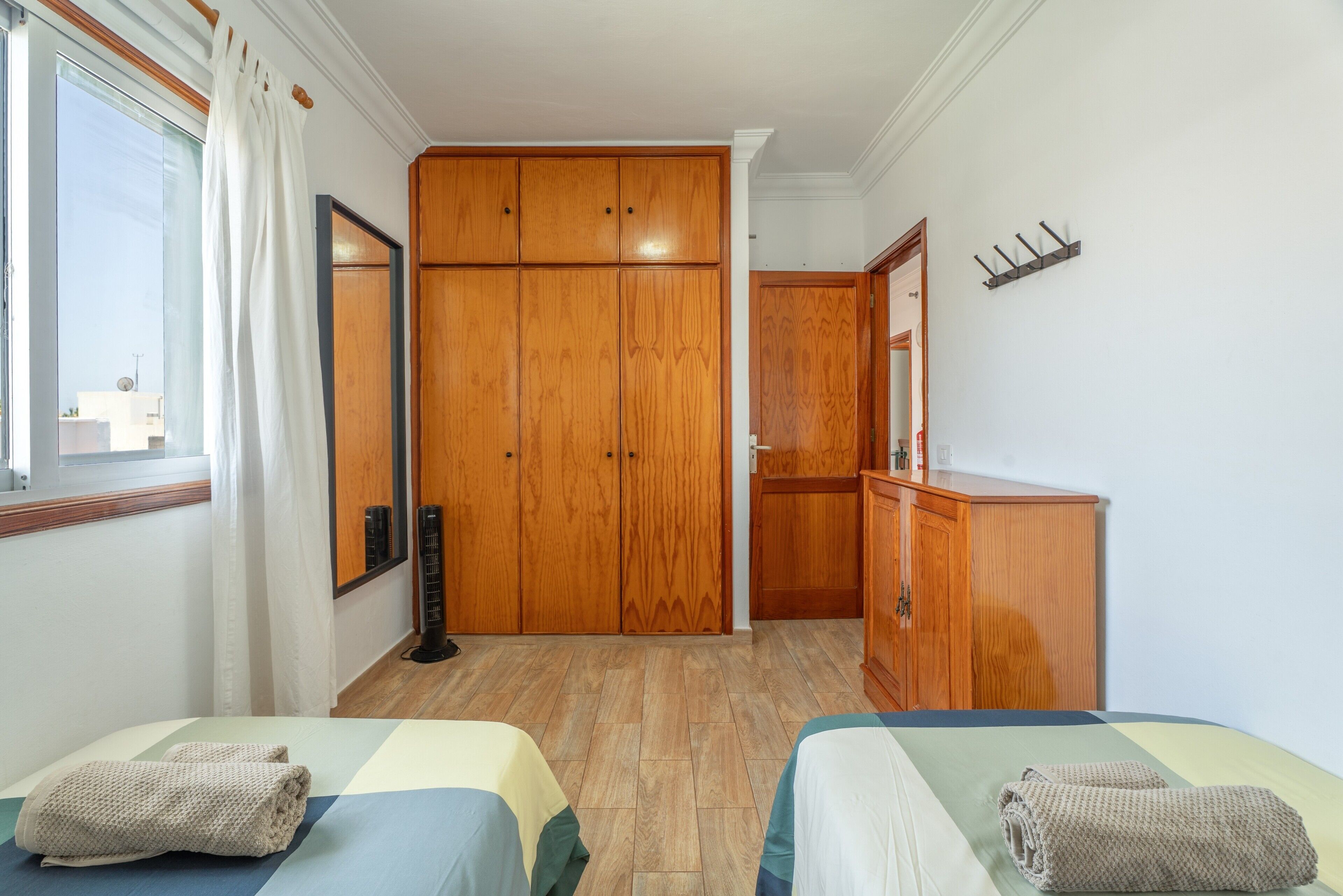 A hotel room with two beds, a wardrobe, a mirror, and a window with curtains.