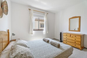 Ein Schlafzimmer mit einem Bett, einem Holzschrank, einem Spiegel und einem Fenster mit Vorhängen.