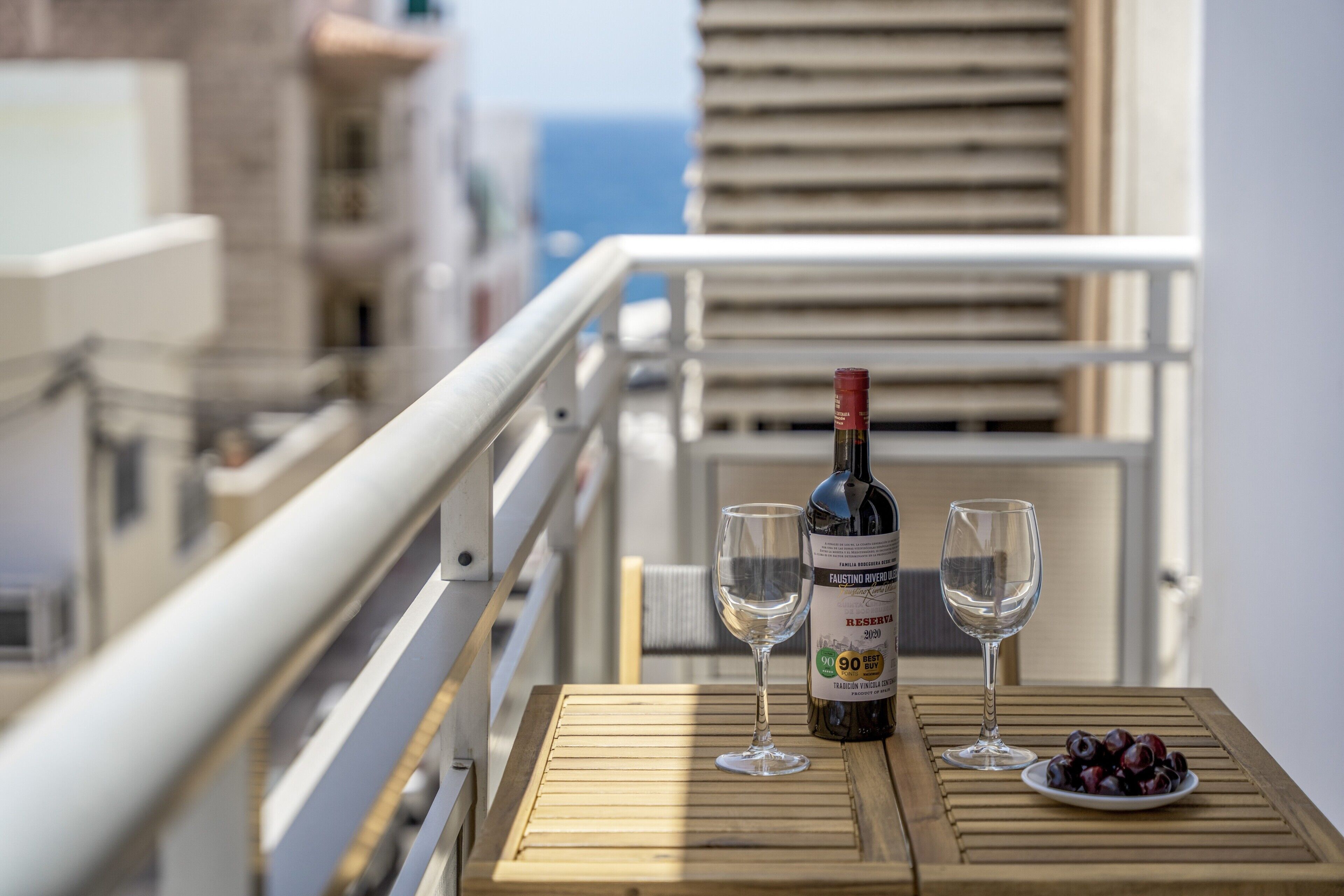 Un balcon avec une table en bois, deux verres à vin, une bouteille de vin et une assiette de raisins.
