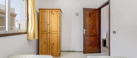 A room with two beds, a wooden wardrobe, a door, and a window with a curtain.